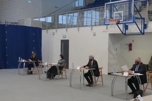 Na zdjęciu znajdują się czterej siedzący w ławkach ludzie. Dwaj mężczyźni i dwie kobiety. Z tyłu widoczne są trybuny. (photo)