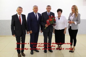 Na zdjęciu znajdują się trzej mężczyźni w garniturach oraz dwie kobiety. Jeden z mężczyzn trzyma w ręku wiązankę kwiatów. (photo)