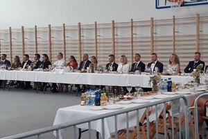 Na zdjęciu widoczni są siedzący za stołami mężczyźni i kobiety odbierający dożynkowe wieńce (photo)