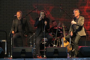 Na scenie znajdują się trzej siedzący i śpiewający mężczyźni. Występ zespołu VOX (photo)