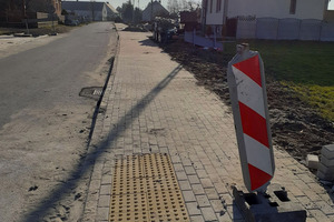 Na zdjęciu znajduje się ulica, budowany chodnik oraz przejście dla pieszych. Na pierwszym planie widnieje znak ostrzegawczy  biało-czerwonego koloru. Znak znajduje się na chodniku. (photo)