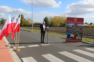 Na środku drogi stoi mężczyzna w garniturze. Po prawej stronie znajduje się roll-up, po lewej flagi Polski (photo)