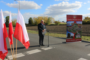 Burmistrz Miejskiej Górki przemawia na środku ulicy. Po prawej stronie roll-up, po lewej flagi Polski (photo)
