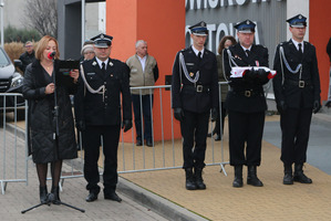 Na zdjęciu stoją czterej strażacy, po lewej stronie przy mikrofonie stoi prowadząca uroczystość konferansjerka (photo)