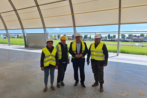Na zdjęciu znajdują się cztery osoby, dwaj mężczyźni oraz dwie kobiety ubrani w odblaskowe kamizelki i kaski. Delegacja pozuje w środku hali sportowej w Konarach. (photo)